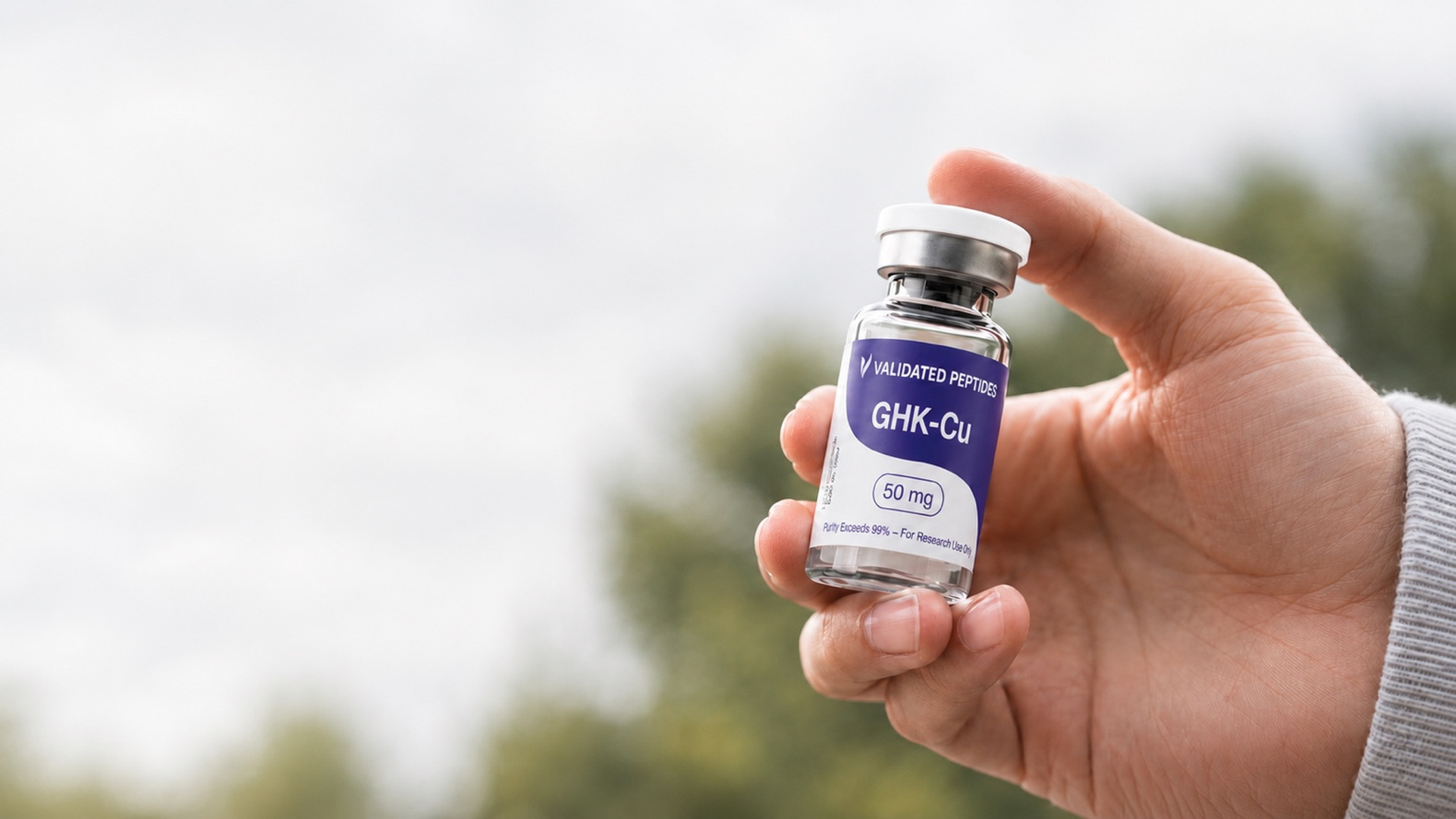 Validated Peptides GHK-Cu research vial held in hand against a natural outdoor backdrop